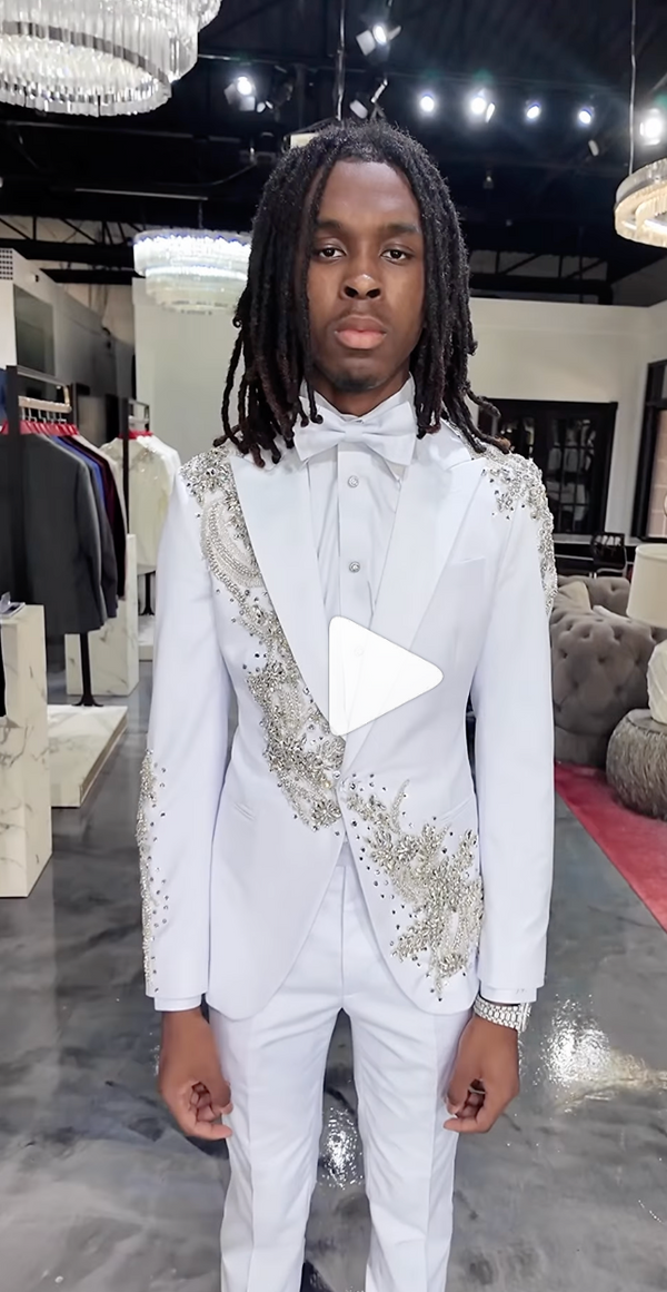 Young man in white suit with silver embroidery in chandelier-lit showroom