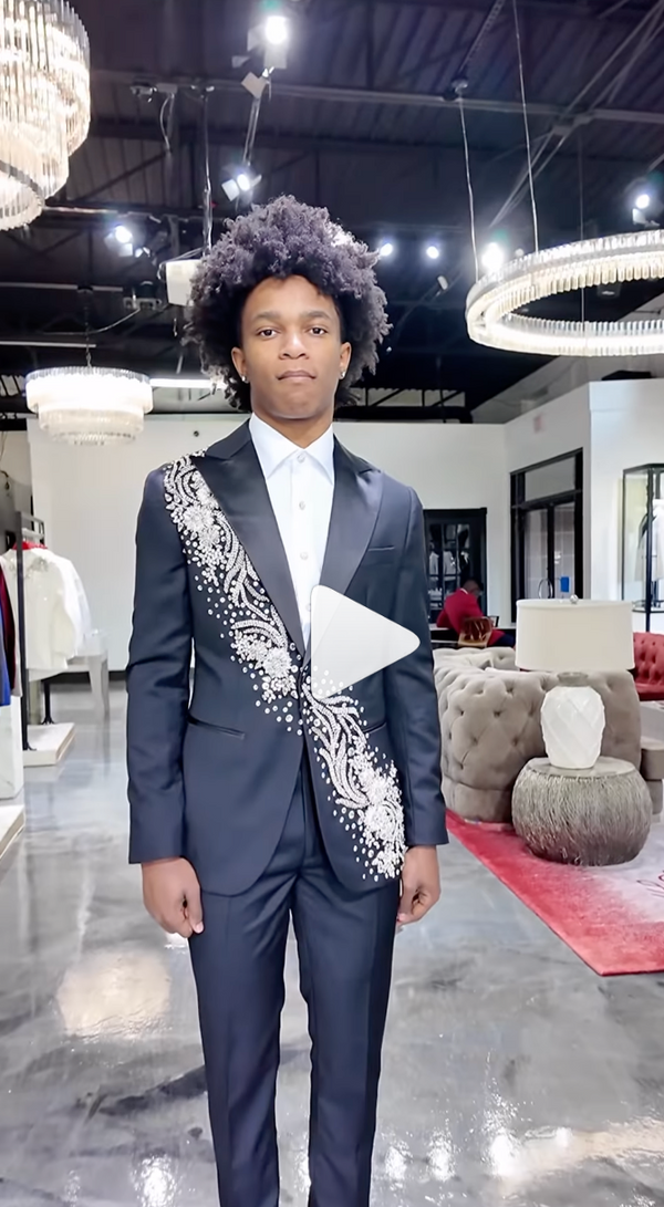 Young man in embroidered black suit standing in elegant chandelier-lit store