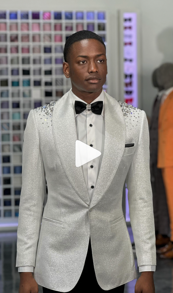 Man in elegant silver tux with bow tie posing near suit sample wall